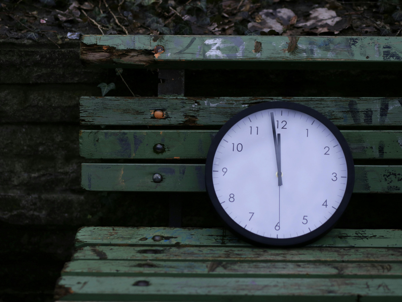 Eine Uhr, die zwölf Uhr anzeigt, liegt auf einer Parkbank.