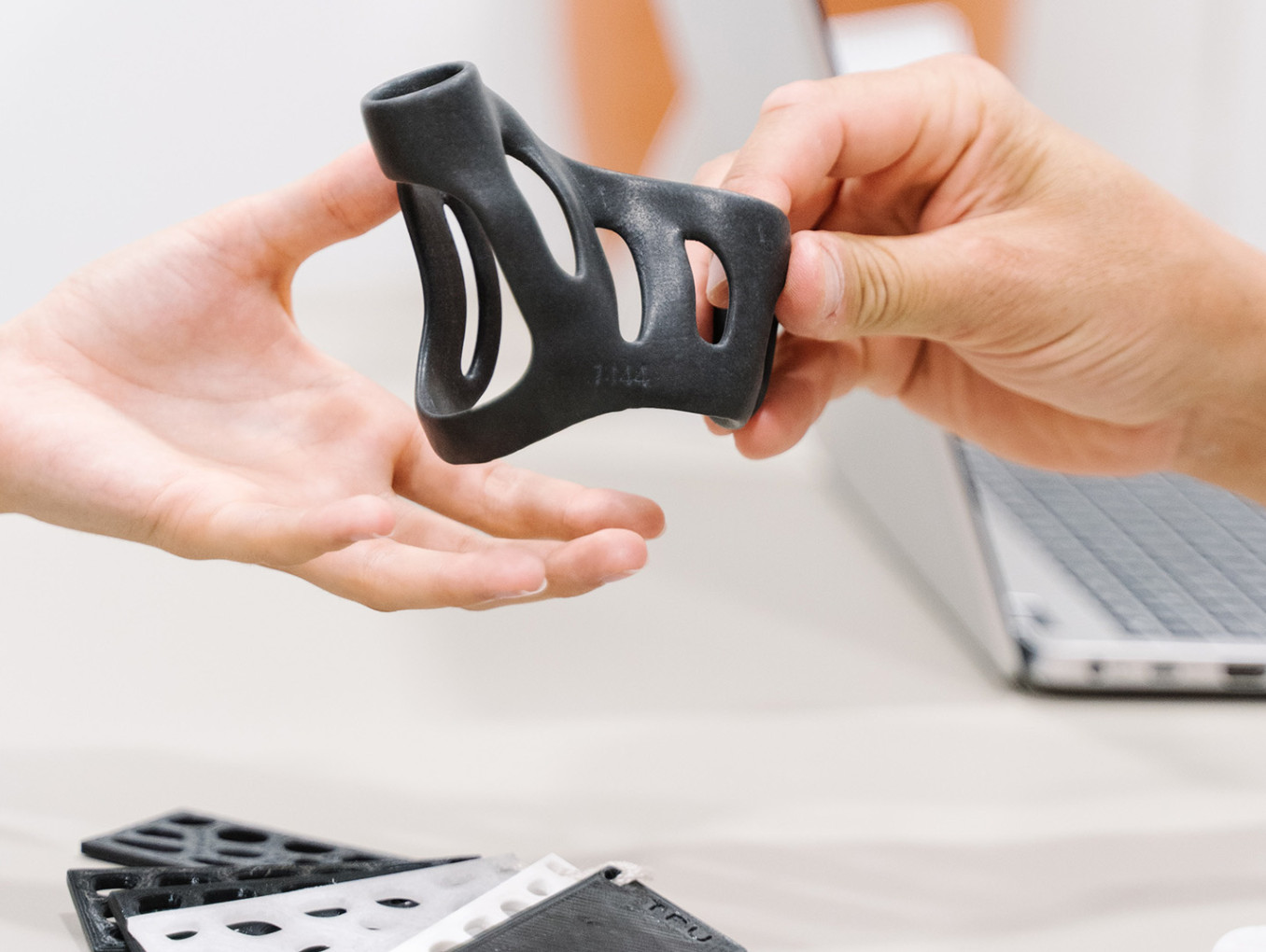 Ein Produkt aus einem 3D Drucker wird von einer Hand an eine weitere Hand gereicht.