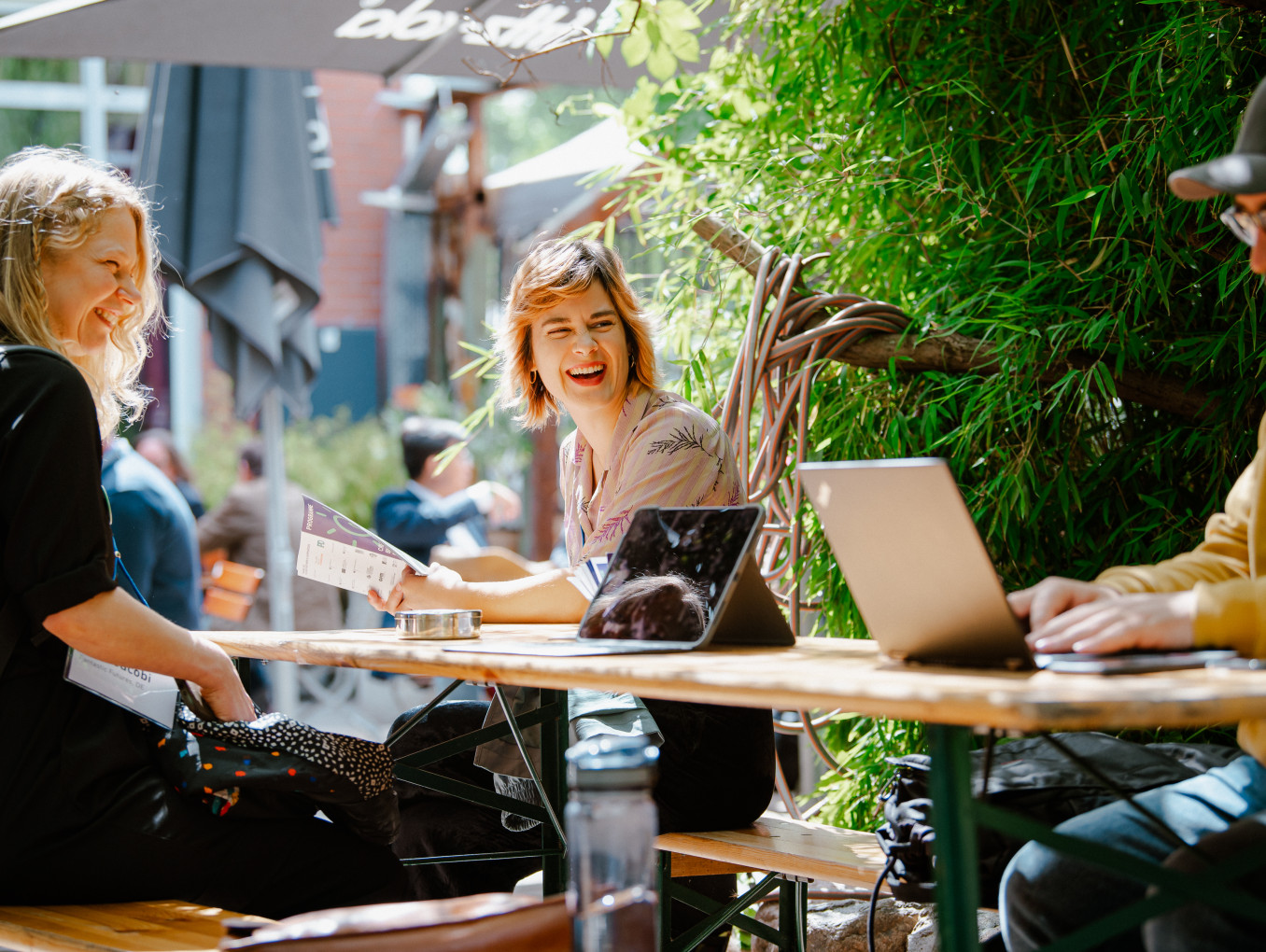 3 people sitting on a table, laughing looking at a laptop 