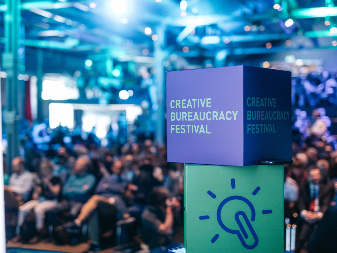people sitting in the back in front of the stage (blurry) and the creative bureaucracy stage merch (dice) is in front 