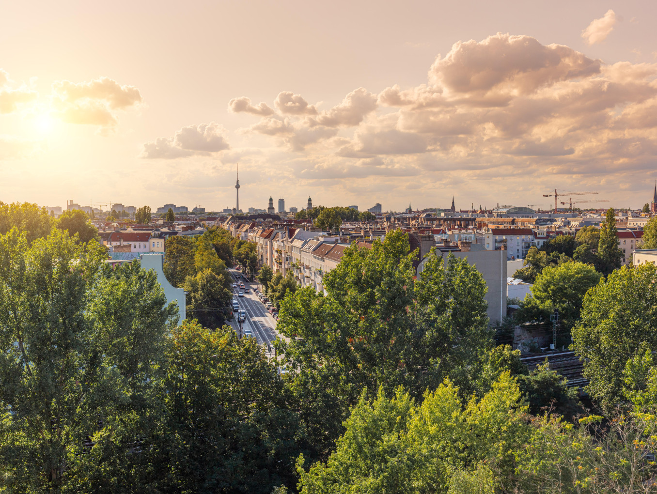 Panorama-Ansicht von Berlin, grün blühende Bäume, vereinzelte Wolken, während die Sonne untergeht