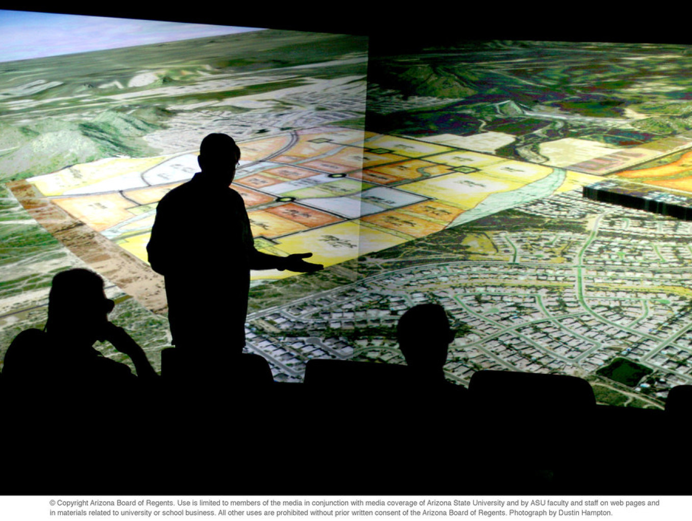 The silhouette of a man in front of a huge screen with fields on it. 