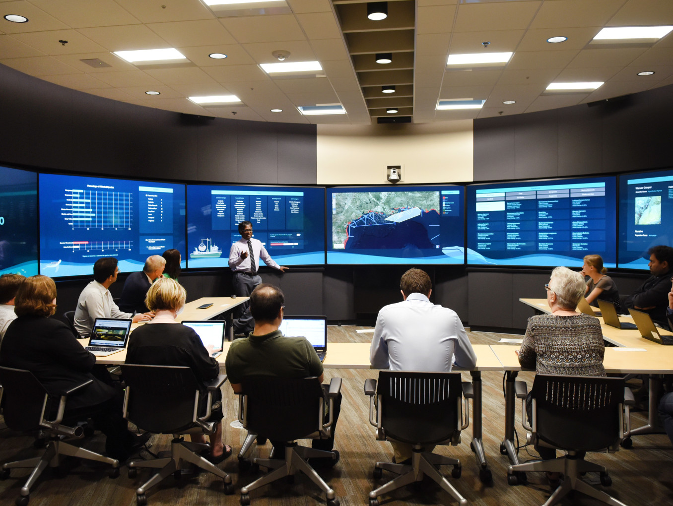 A group of people sit in front of screens. 