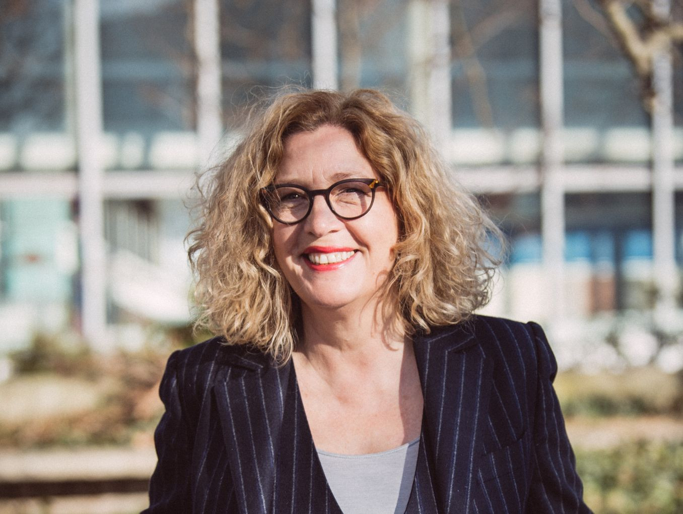 Martina Löw stands in a suit and glasses with her hands in her pockets. 