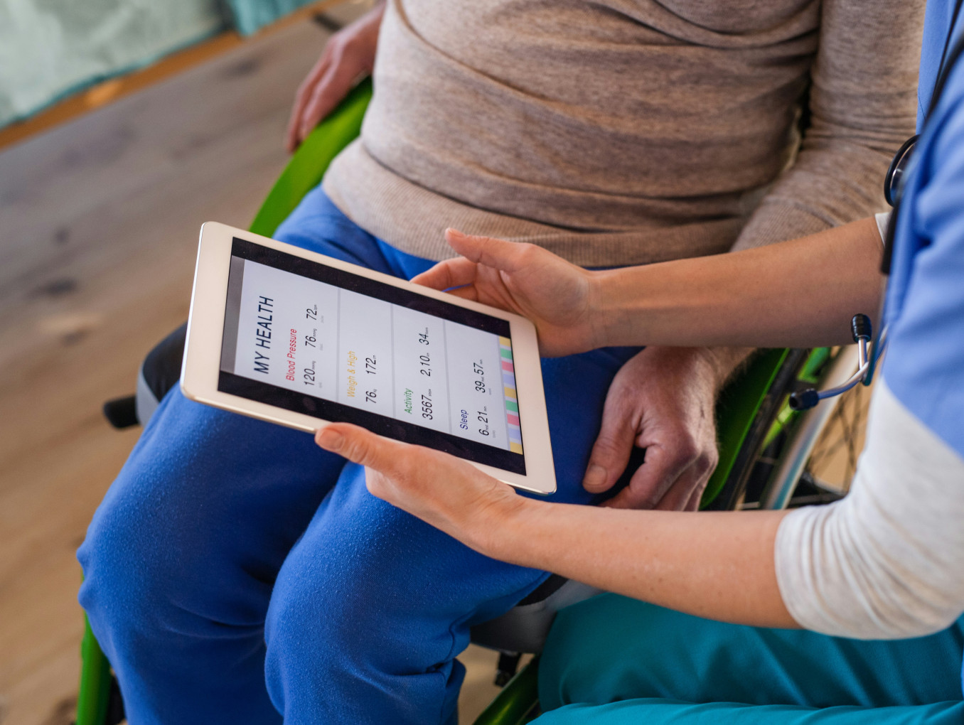A caretaker using a device to show an elderly patient their health status. 
