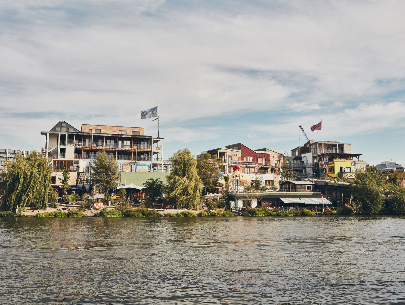 A set of buildings covered in greenery by a big river. 