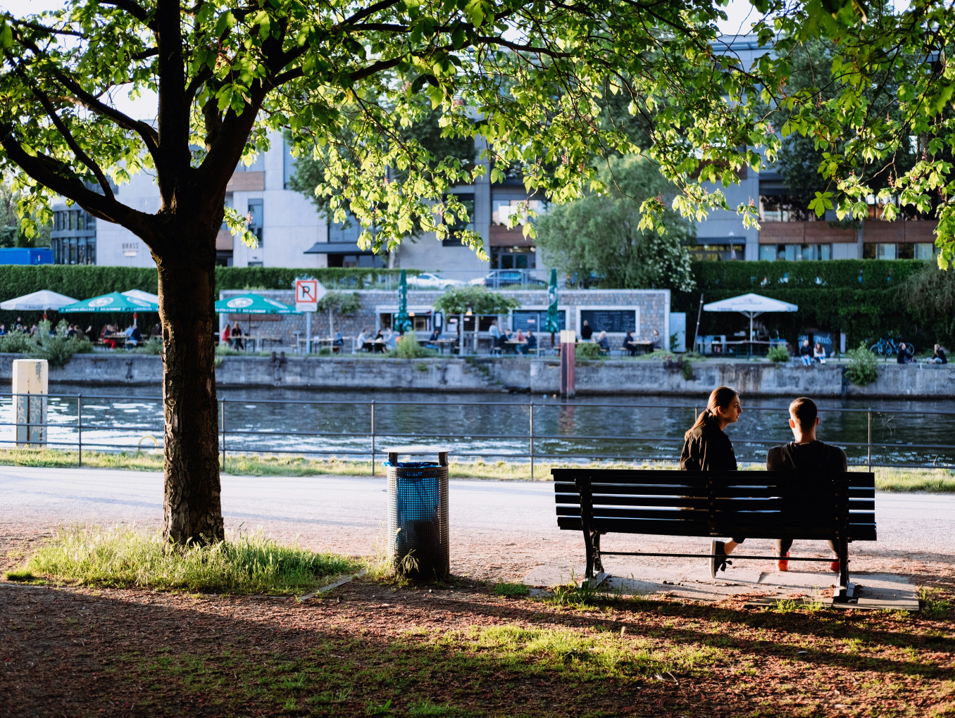 Two people on a park bench sit by the Spree. 