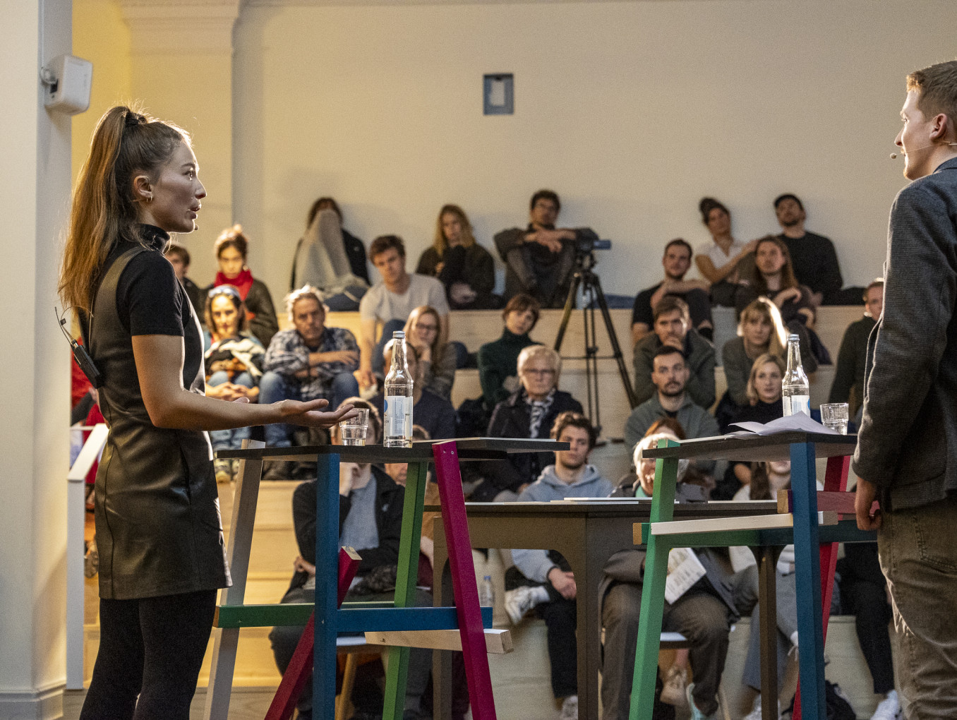 Two people facing one another stand in front of an audience. 