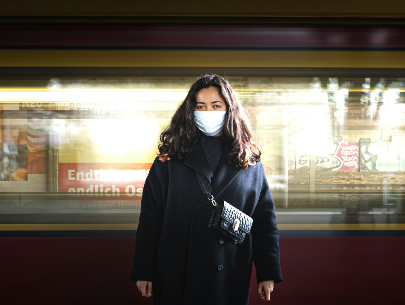 A woman with a mask stands in front of a moving Berlin train.