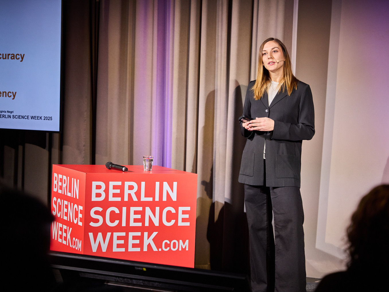 A woman gives a talk next to a red cube. 