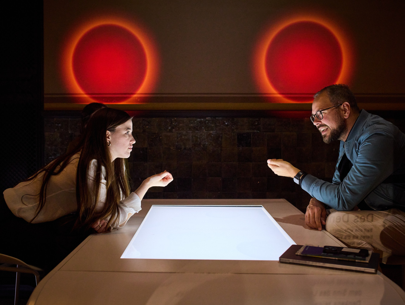 Two people speaking over a table with red orbs over their heads