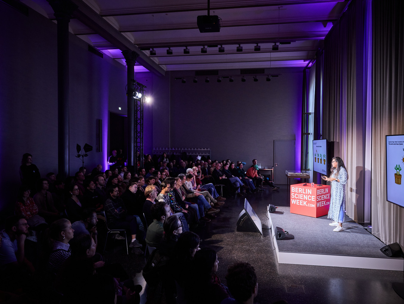 A woman stands on a stage sharing her research about plants. 
