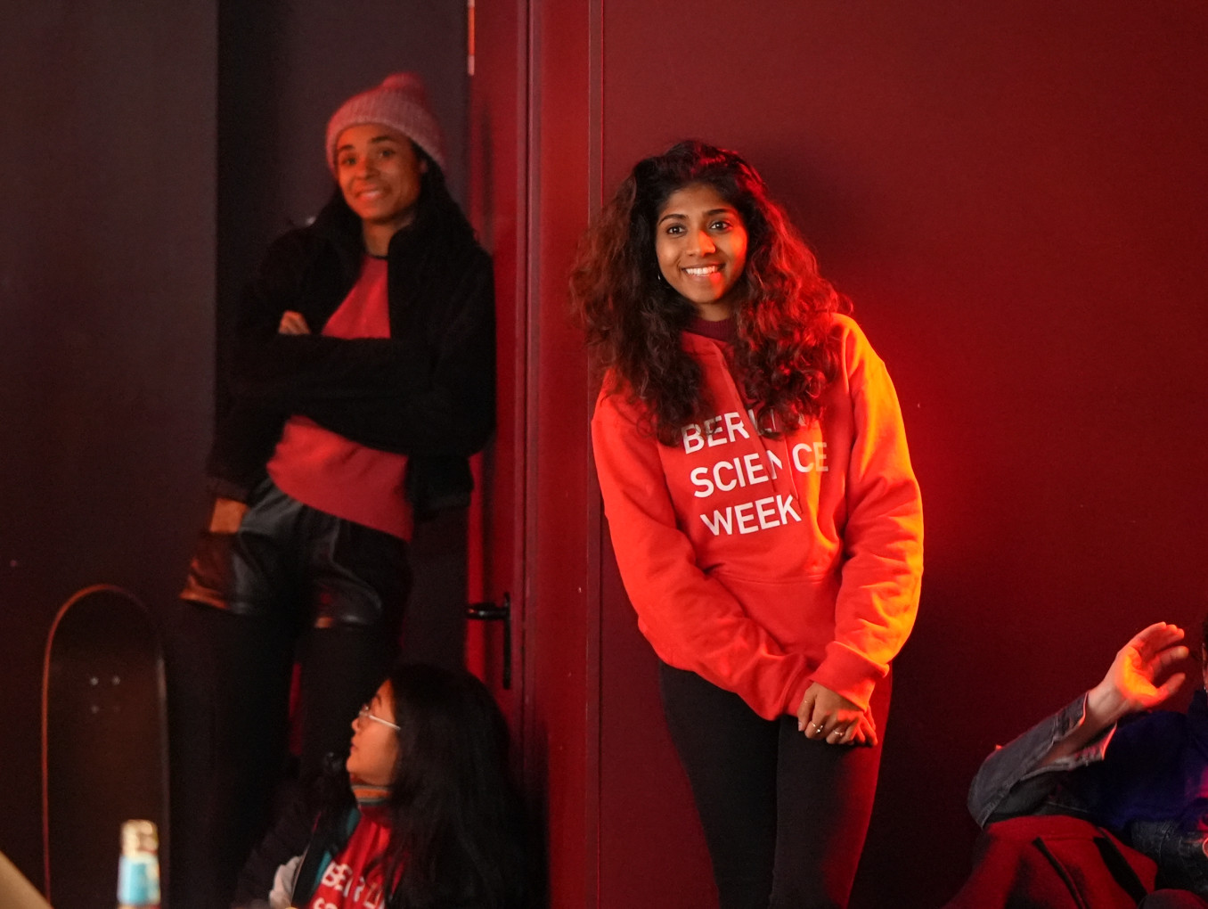 A young woman leans against a wall and smiles.