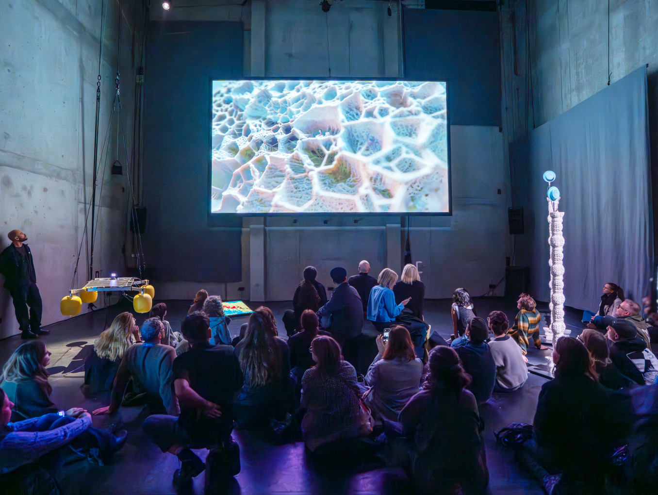 A group of people staring at a big screen above them. 