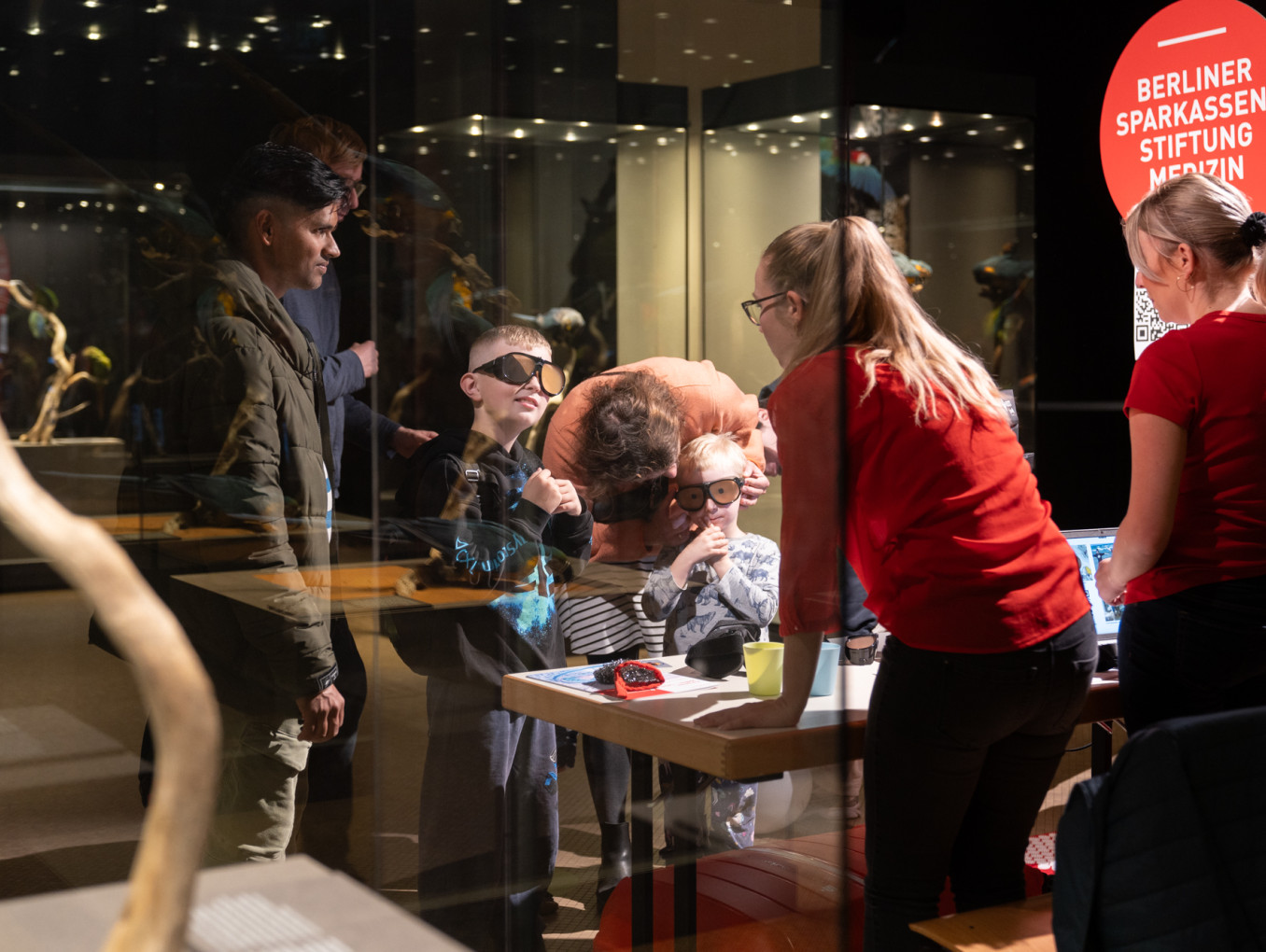 Two children and various adults wear glasses at an exhibition booth.