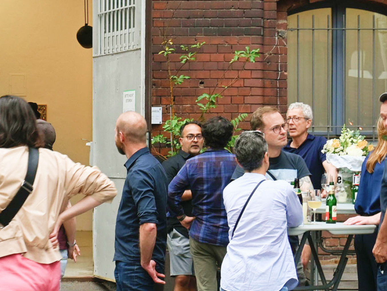 Eine Vernissage im Hinterhof der Urbanstraße 116 in Berlin, zahlreiche Menschen unterhalten sich in Gruppen, stehen mit Getränken oder sitzen an Tischen.