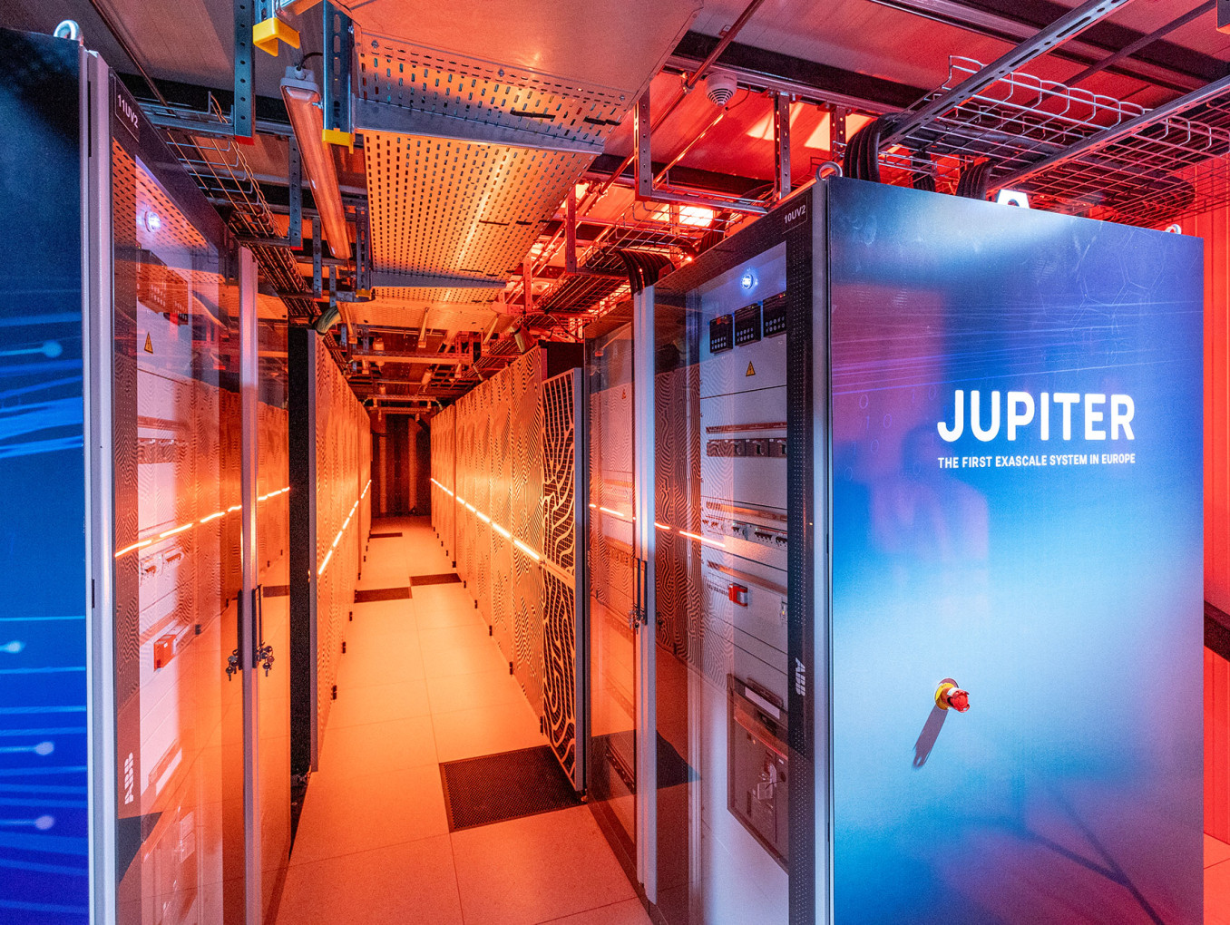 Zwei große, vertikale Rechnerschränke mit den Aufschriften 'JUPITER' in blauen und weißen Farbtönen. Der Raum ist mit orangefarbenem Licht beleuchtet.