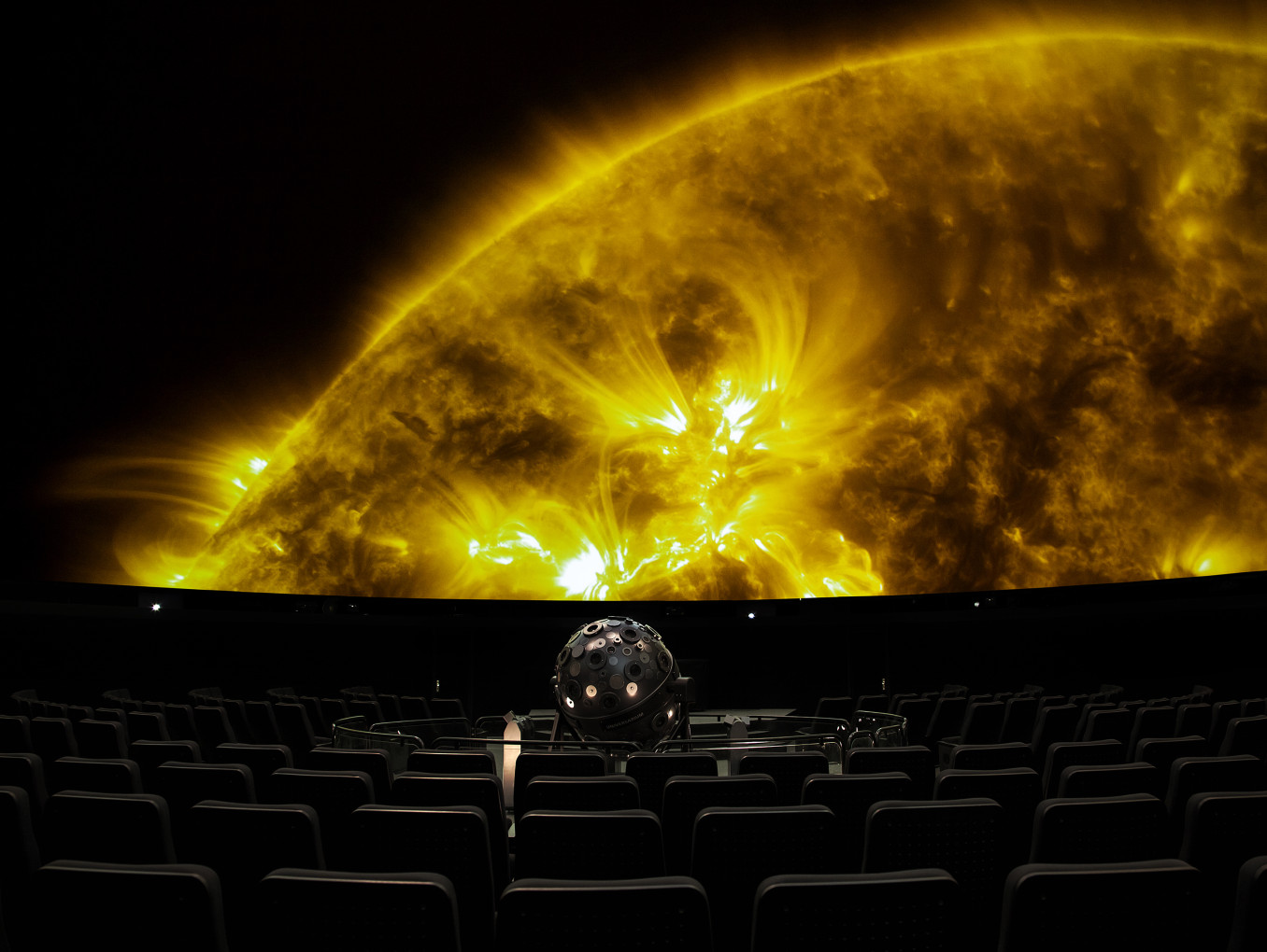 Projektion eines Teils einer gelben Sonnenoberfläche in einem Planetariumssaal mit einem Sternenprojektor im Vordergrund