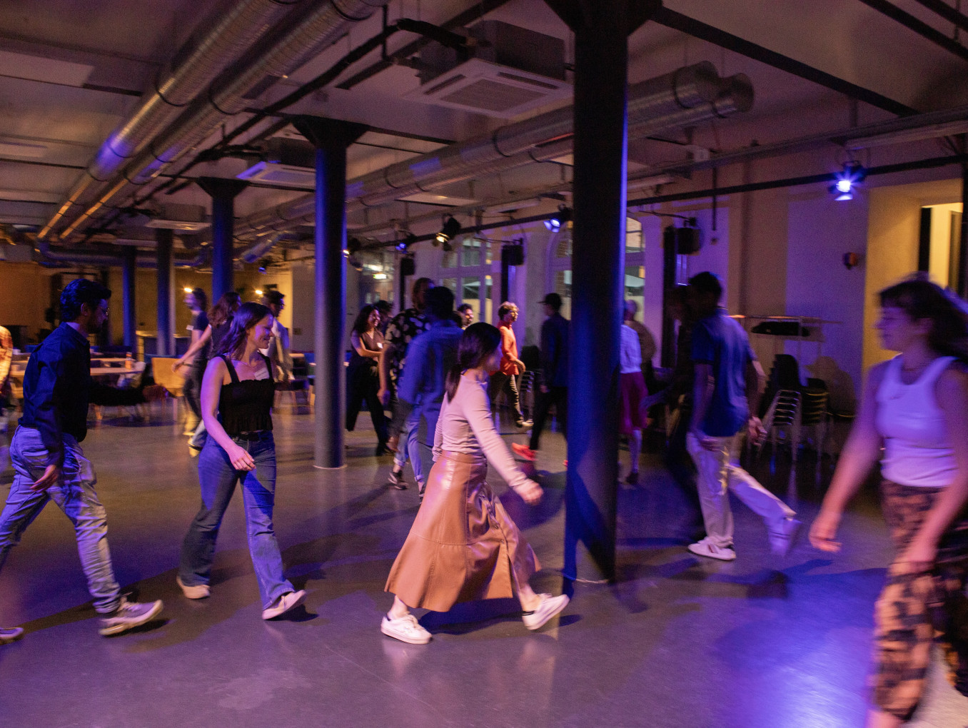 Workshop participants moving around a room with dim purple lighting 