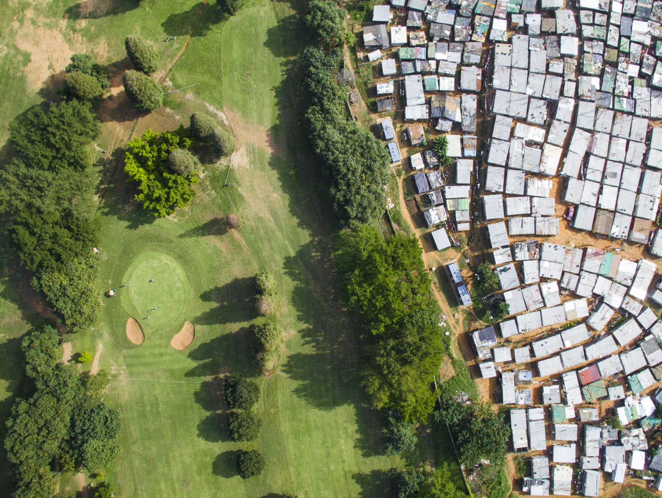 A green golf course with a sprawling informal settlement next to it. 