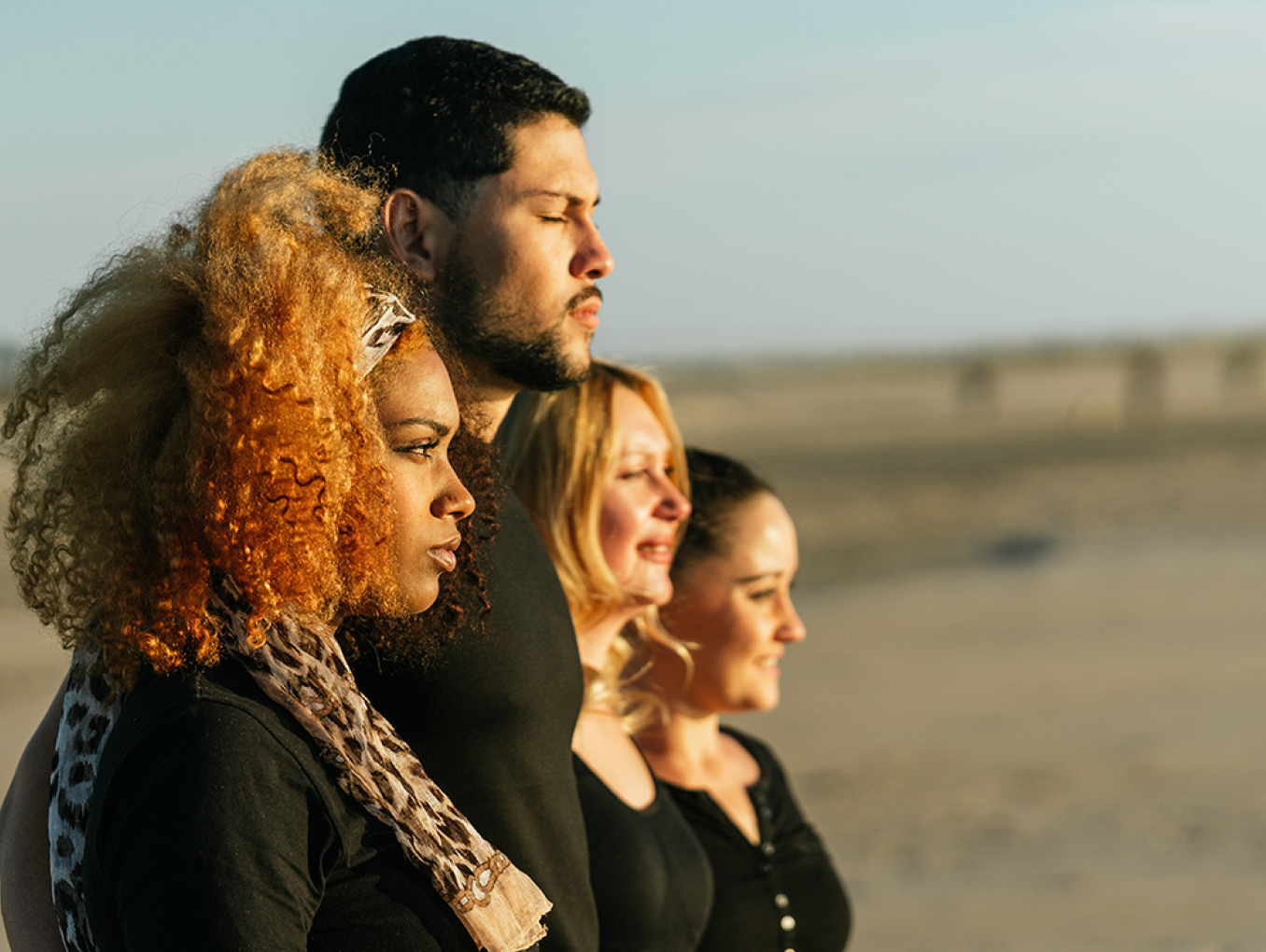 Four people standing and looking at the horizon, with a beach in the background