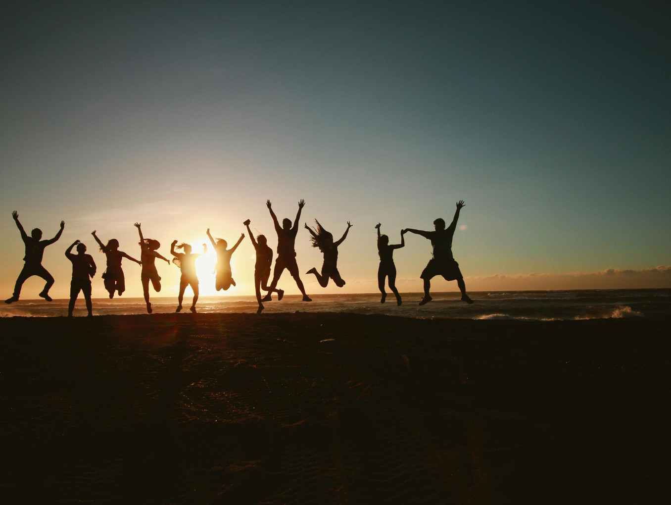 people jumping up, raising their arms while the sun goes down