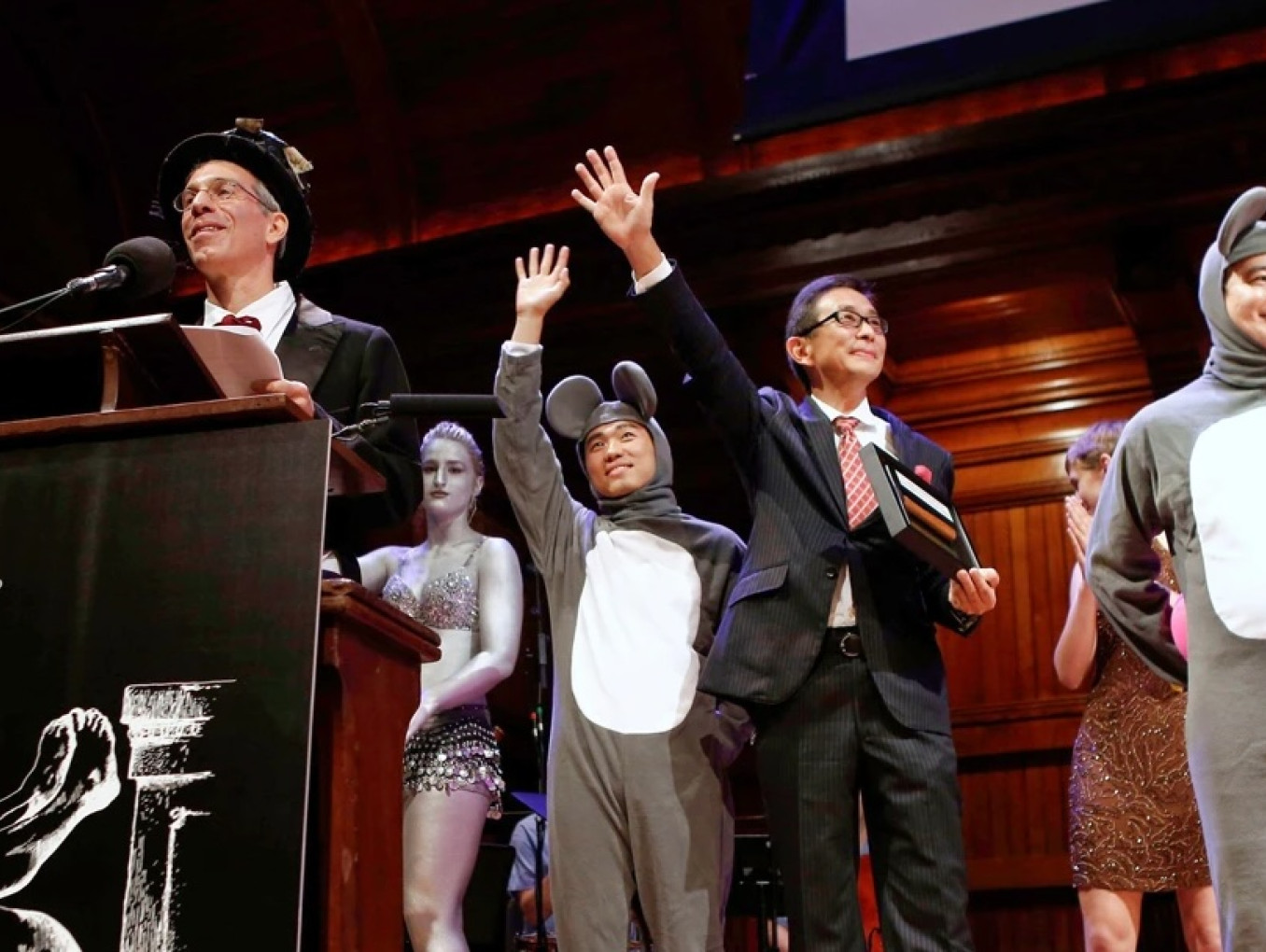 Marc in top hat at podium alongside men dressed as mice and women in silver paint.