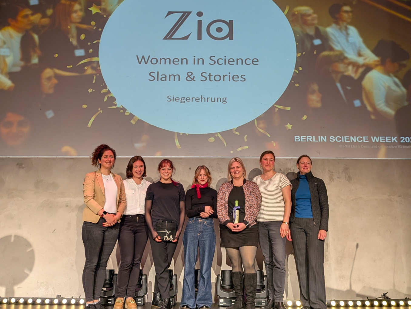 Gruppenfoto von sieben Frauen auf einer Bühne vor einer Leinwand mit dem Schriftzug „Zia Women in Science Slam & Stories – Siegerehrung“.