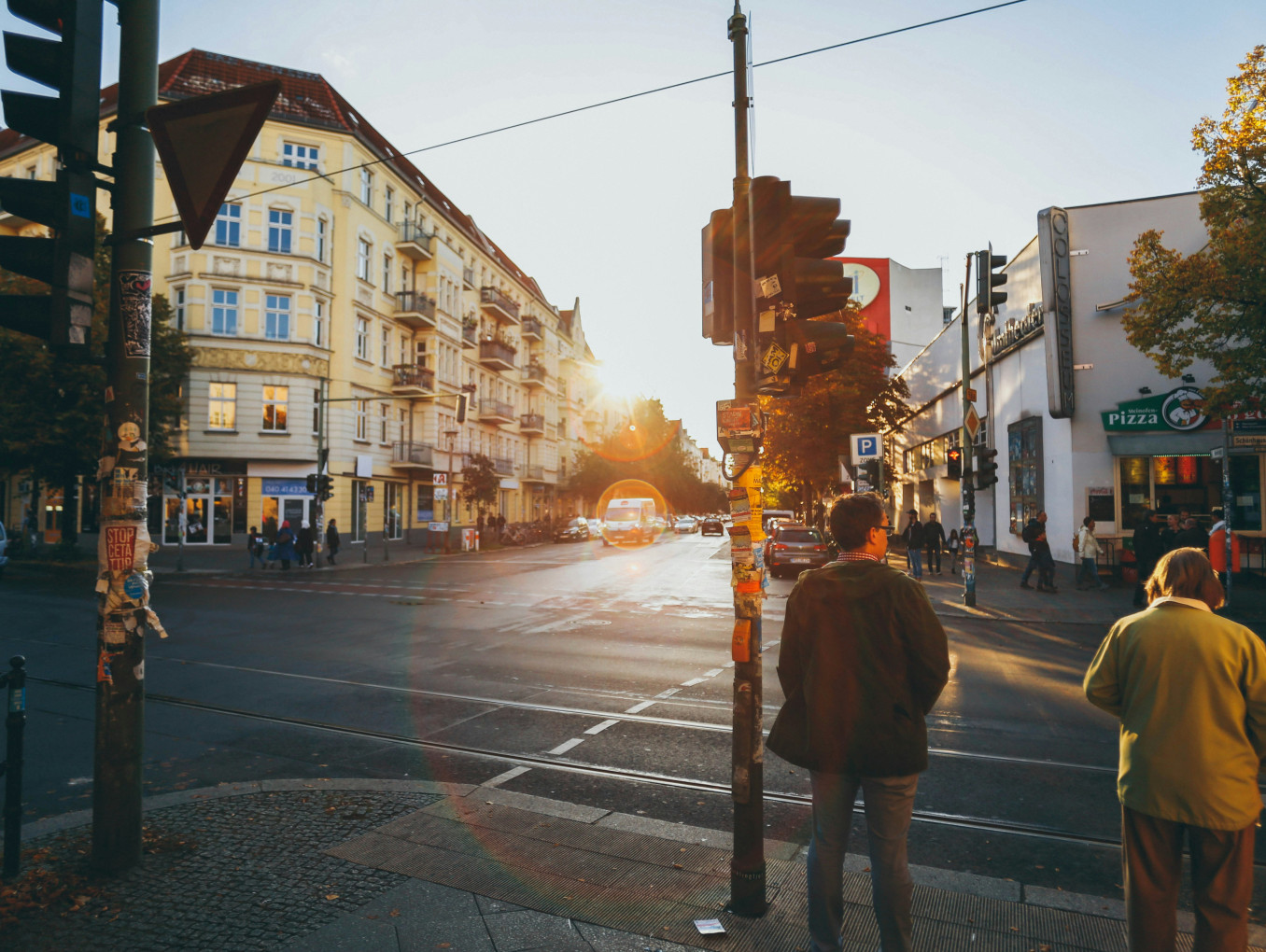 Straßenszene an der Schönhauser Allee mit Fußgängern an einer Ampel und Gebäuden im Hintergrund bei Sonnenuntergang