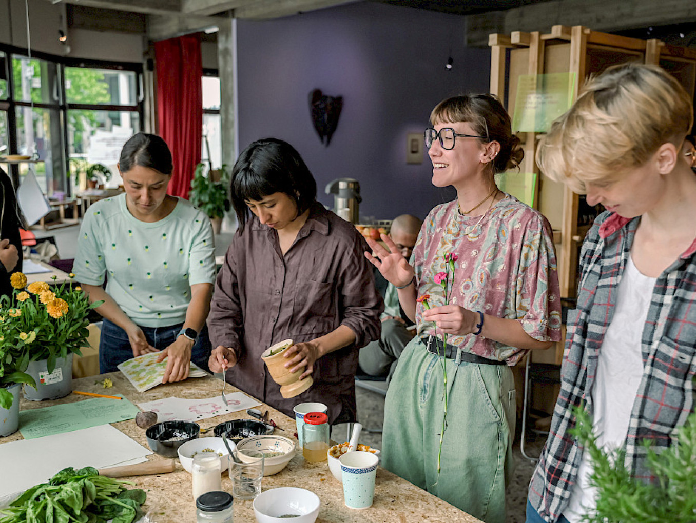 Participants work at a table covered in plants and flowers during a hands-on workshop at SAVVY Contemporary, Berlin.