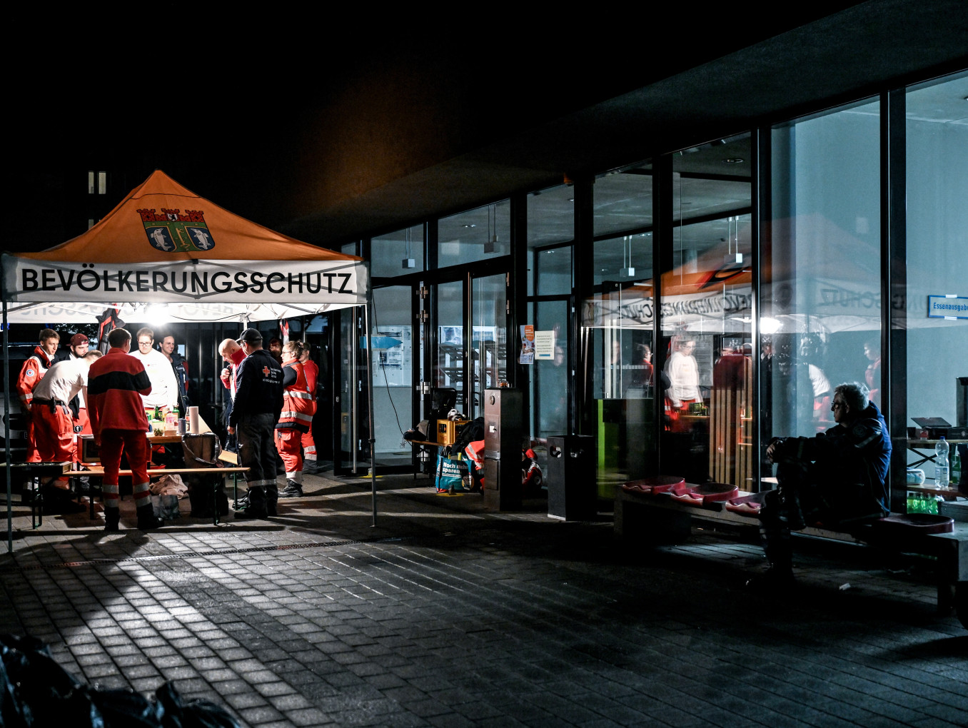 Zelt mit der Aufschrift "Bevölerkungsschutz" auf einer dunklen Straße neben einem schwach beleuchteten Gebäude. 