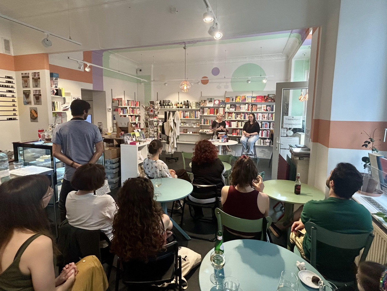 A group of people sitting down around tables, with their backs to the camera, in a book store, listening to a talk