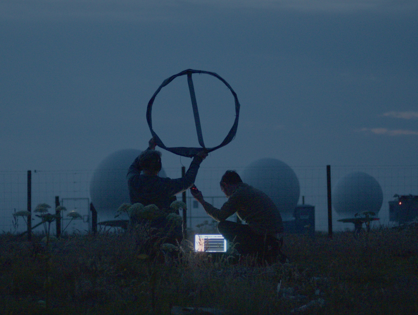 Image from Song for the Cosmos showing artist Edwin Mingard and musician Gina Ritch at dusk, listening to a spaceport's ground control using an experimental aerial