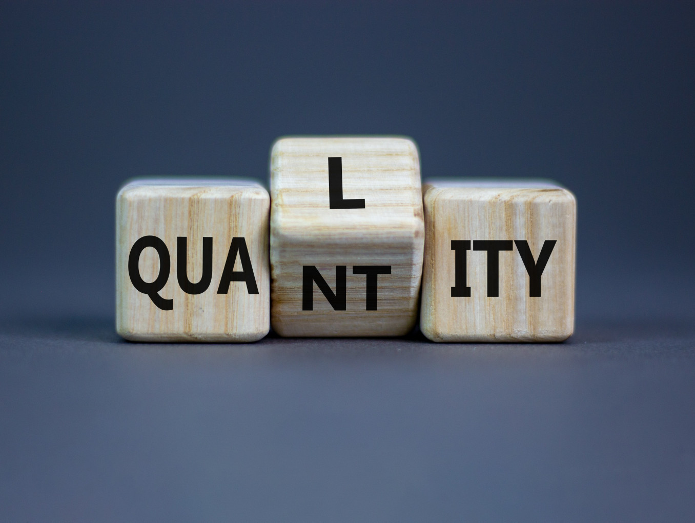 A picture with wooden letters which are simultaneously spelling "Quality" and "Quantity".
