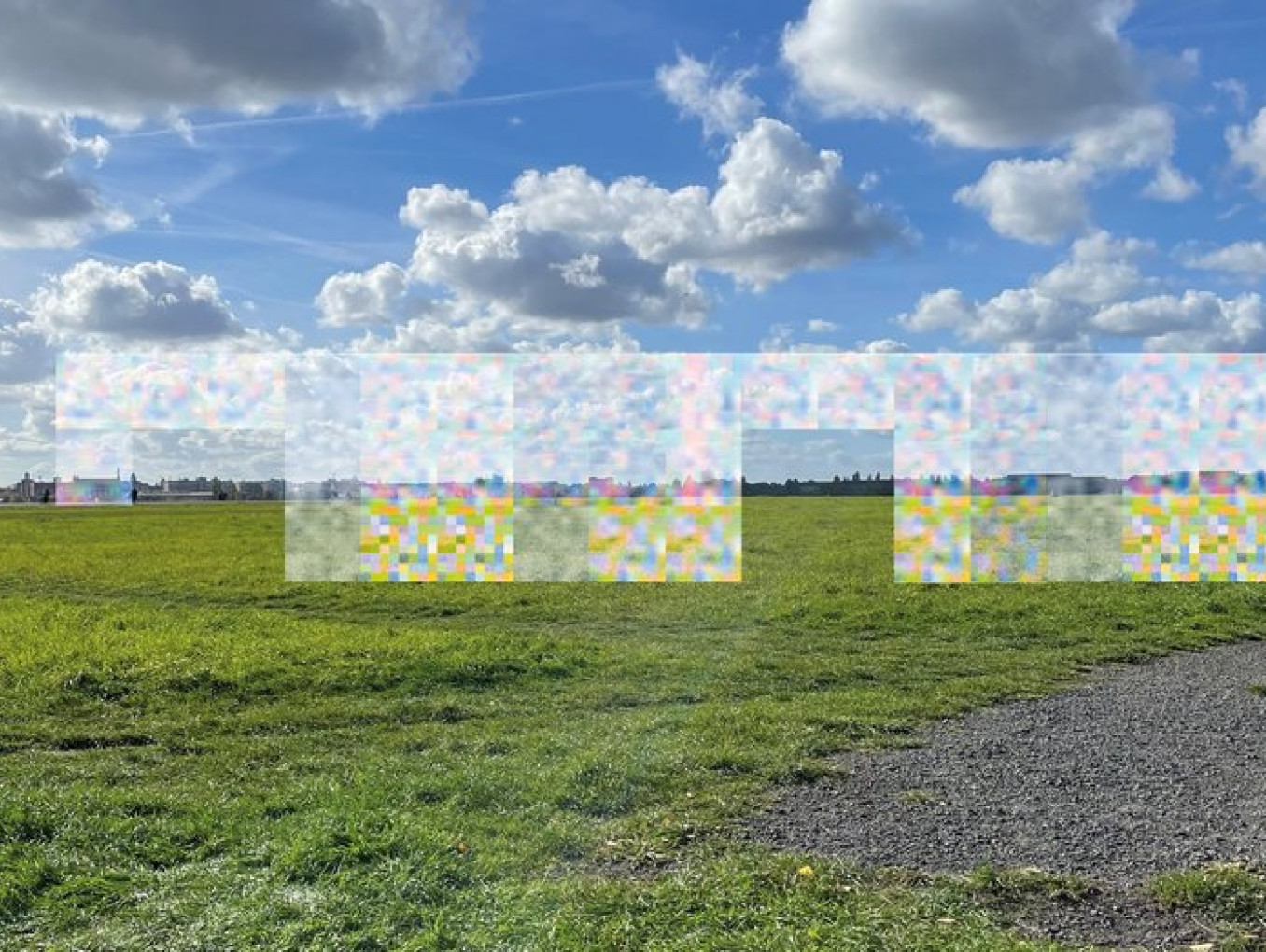 Eine weitläufige grüne Wiese unter einem blauen Himmel mit weißen Wolken. In der Mitte sind bunte, verpixelte Kästchen, die den Hintergrund verzerren.
