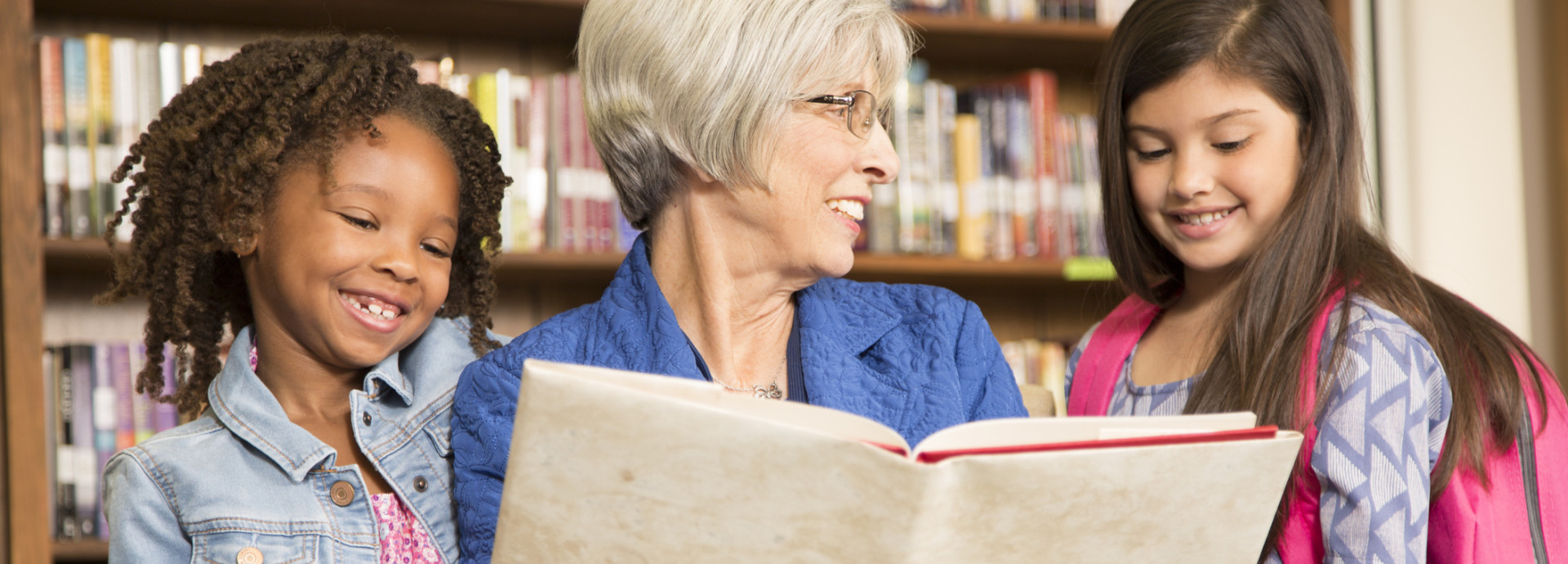 Frau liest zwei Kinder aus einem Buch vor
