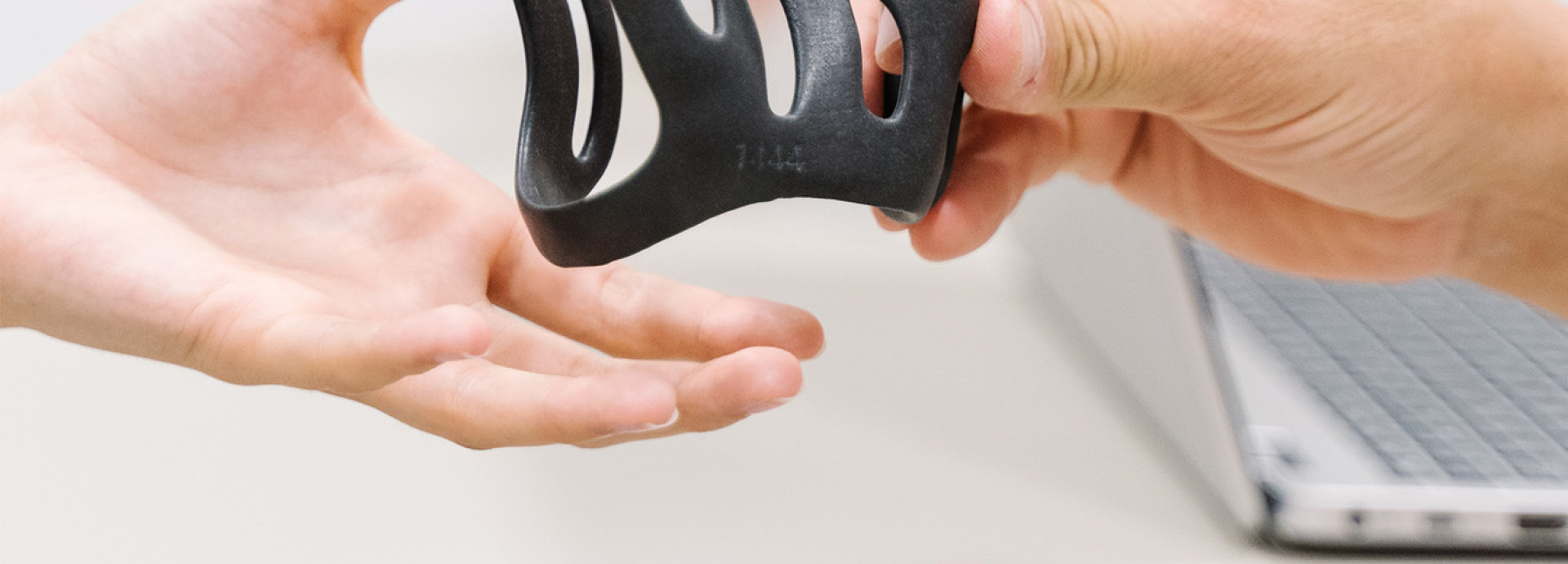 Ein Produkt aus einem 3D Drucker wird von einer Hand an eine weitere Hand gereicht.