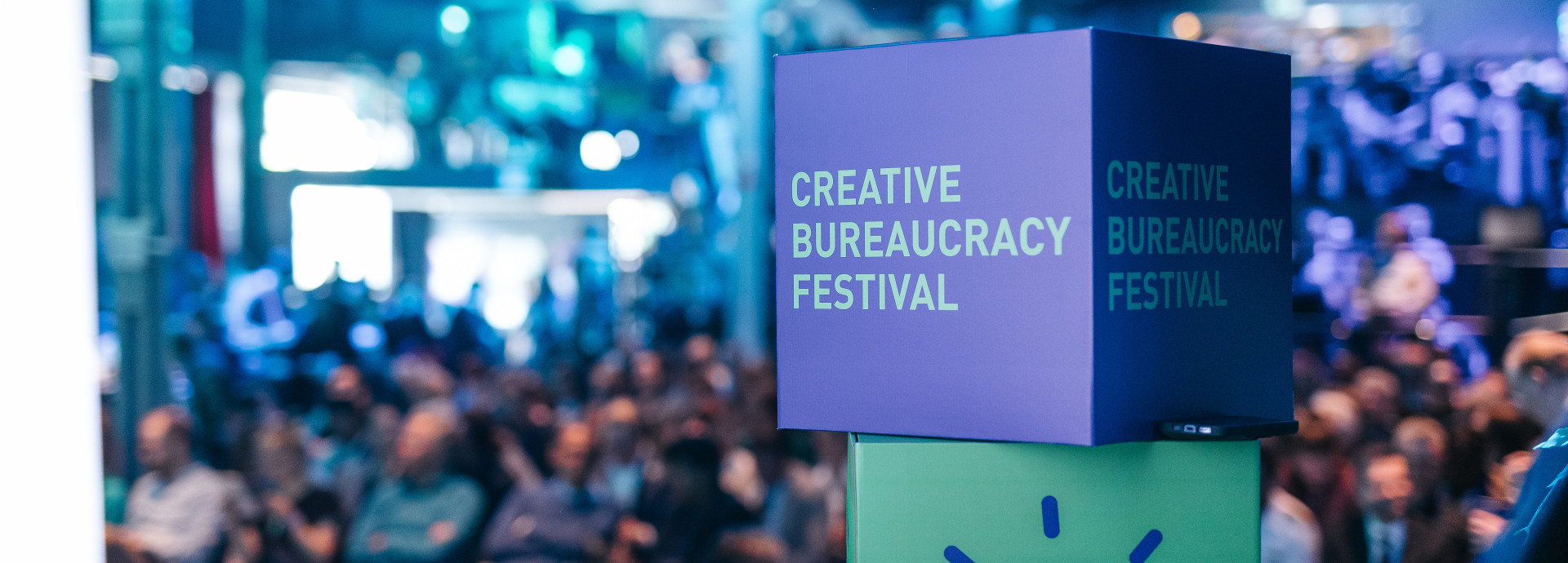 people sitting in the back in front of the stage (blurry) and the creative bureaucracy stage merch (dice) is in front 