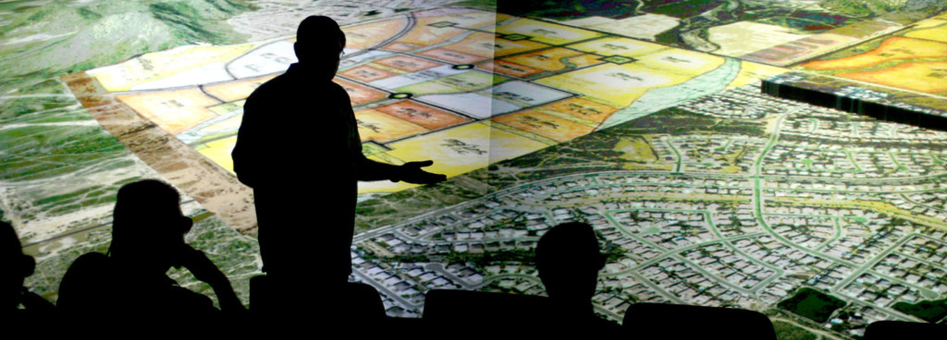 The silhouette of a man in front of a huge screen with fields on it. 
