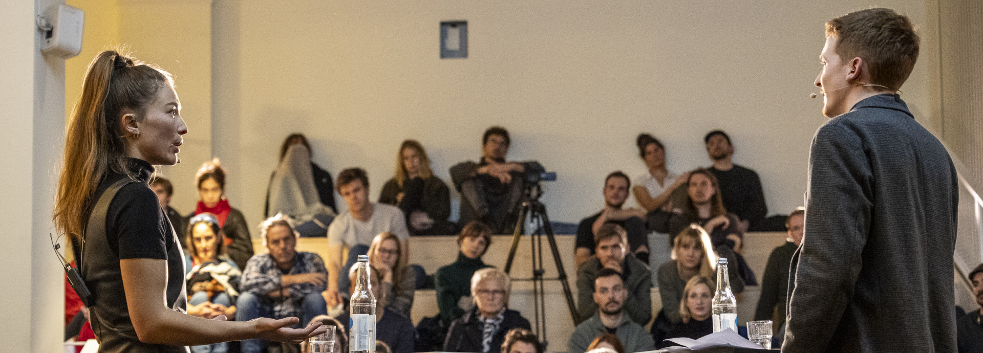 Two people facing one another stand in front of an audience. 