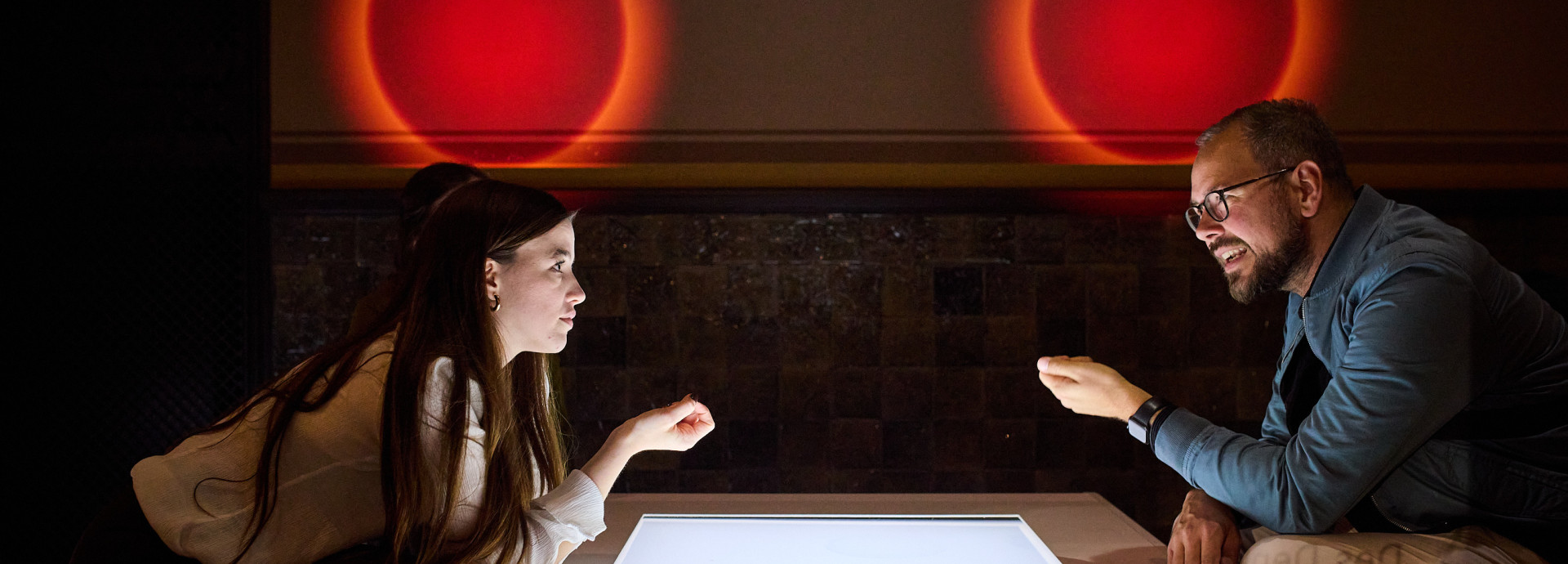 Two people speaking over a table with red orbs over their heads