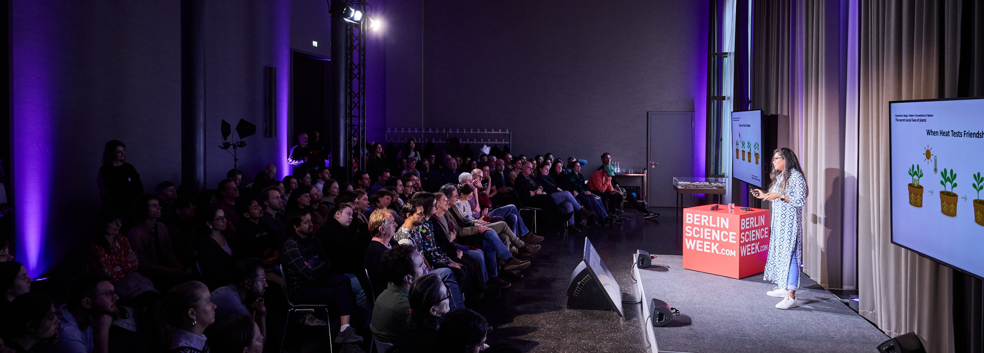 A woman stands on a stage sharing her research about plants. 