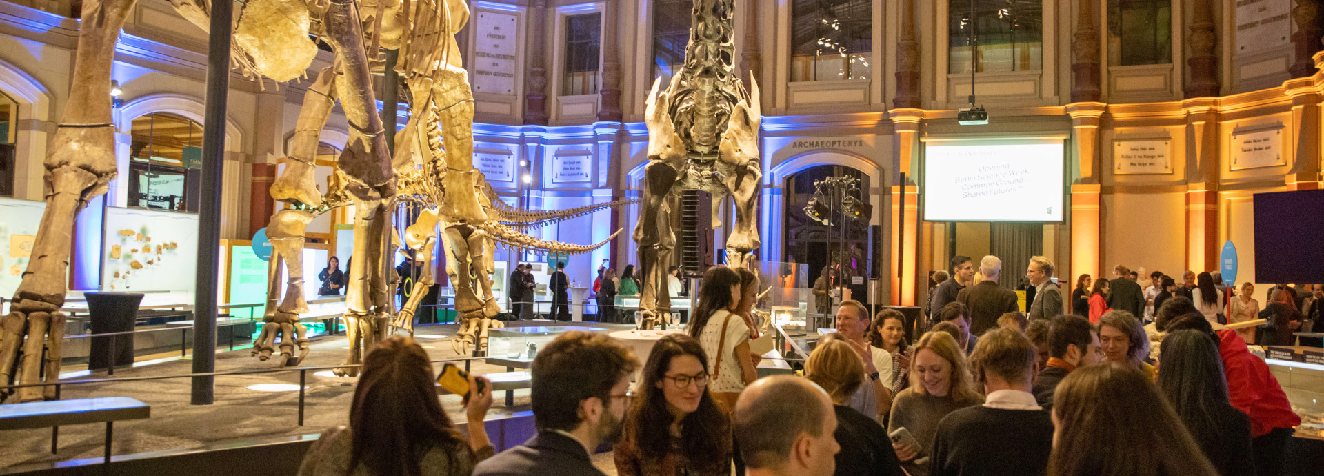 A group of people stand in a museum in the evening.