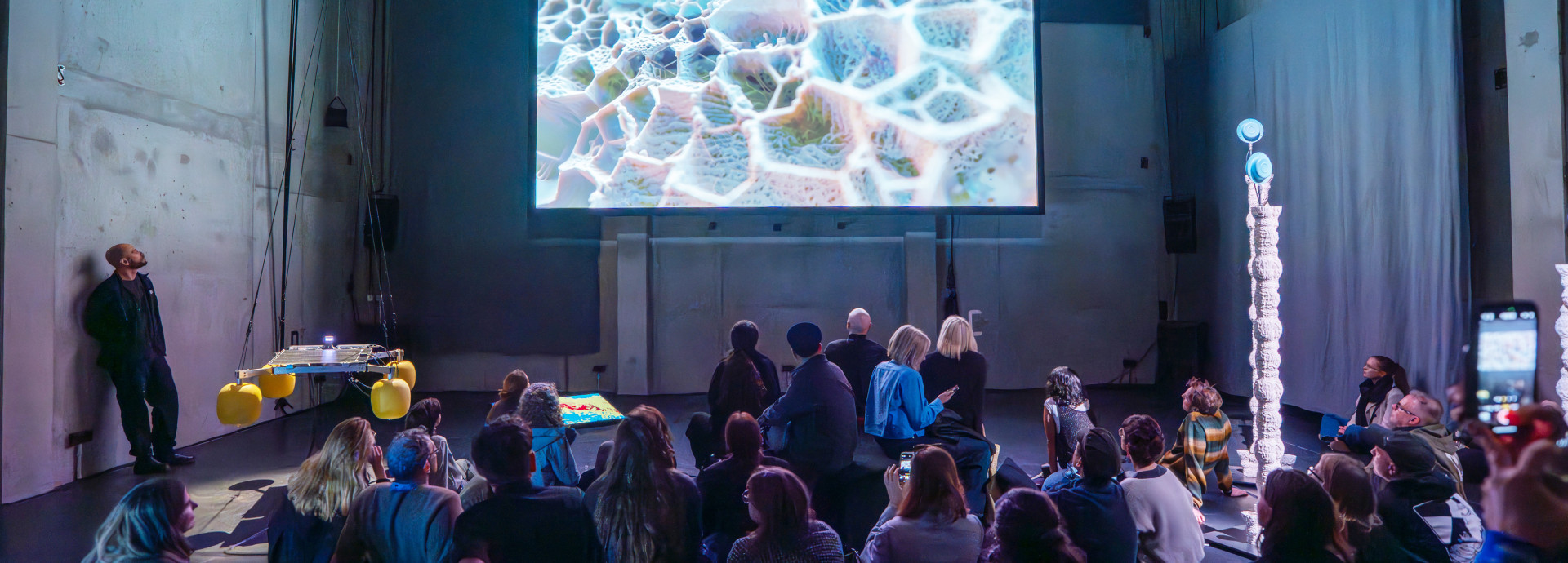 A group of people staring at a big screen above them. 