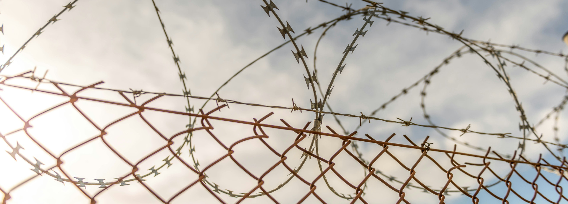 Bild eines Stacheldrahtzauns mit dunklen Wolken und der durchbrechenden Sonne