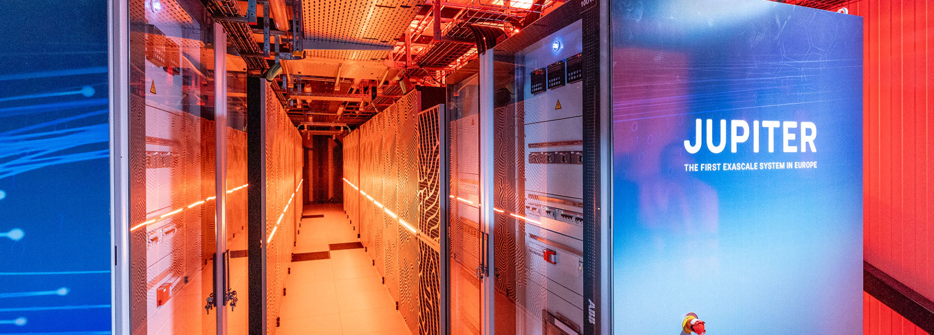 Zwei große, vertikale Rechnerschränke mit den Aufschriften 'JUPITER' in blauen und weißen Farbtönen. Der Raum ist mit orangefarbenem Licht beleuchtet.
