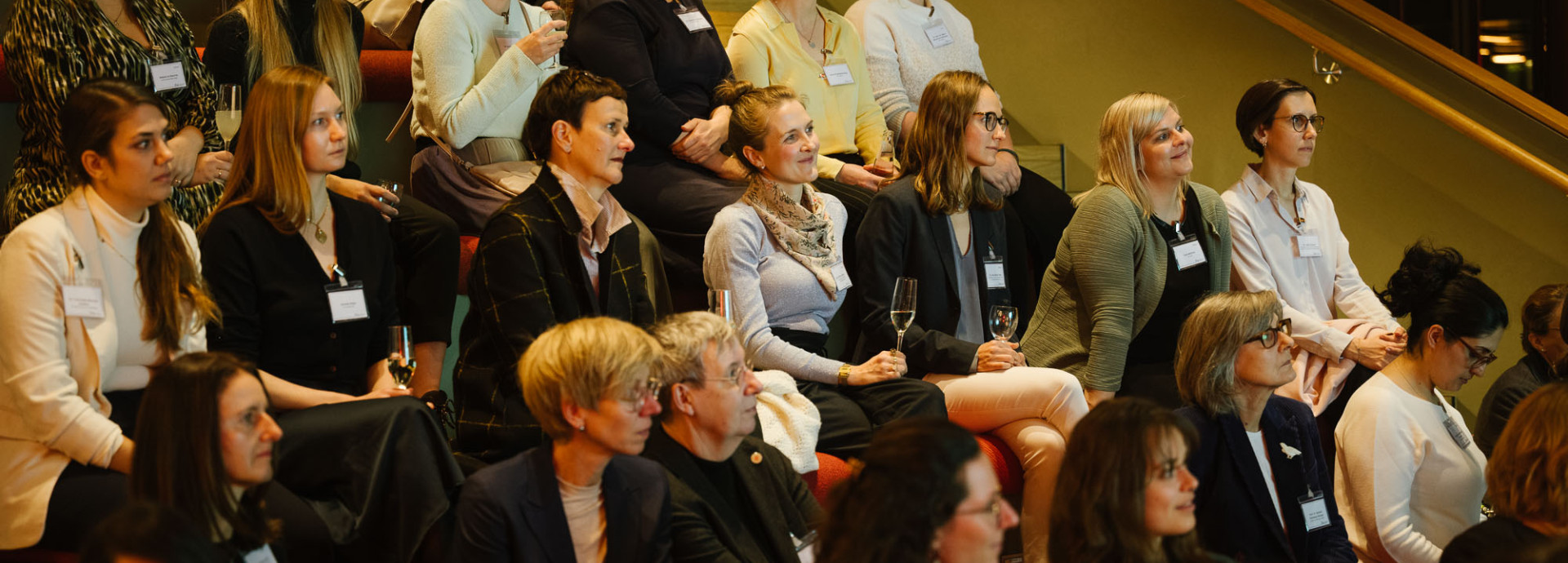 A attentive crowd of women watching from  a seating area.