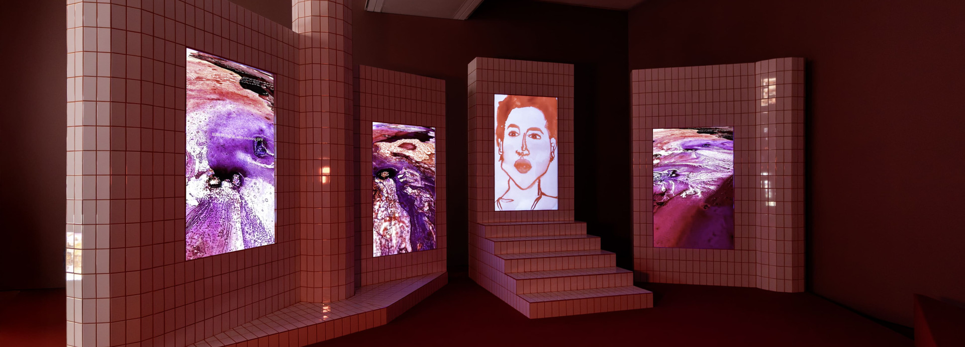 Four vertical screens in white tiles with red grout show videos of watercolor images and a portrait. 