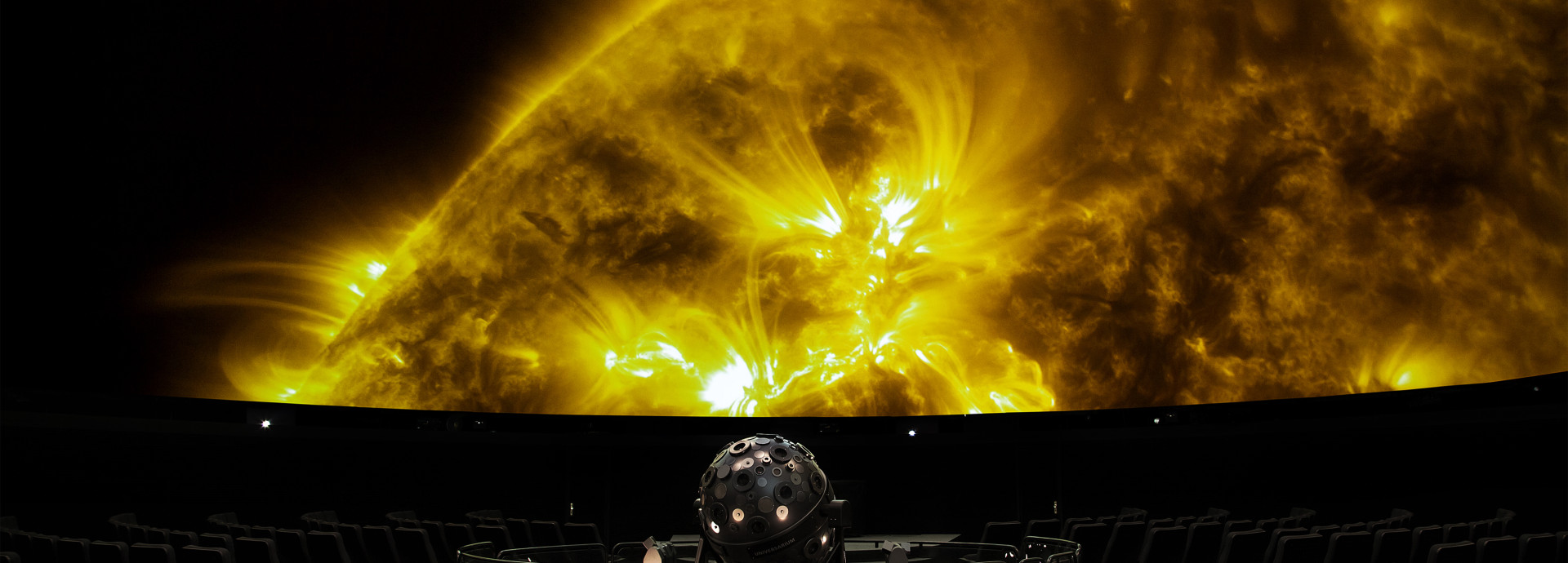 Projektion eines Teils einer gelben Sonnenoberfläche in einem Planetariumssaal mit einem Sternenprojektor im Vordergrund