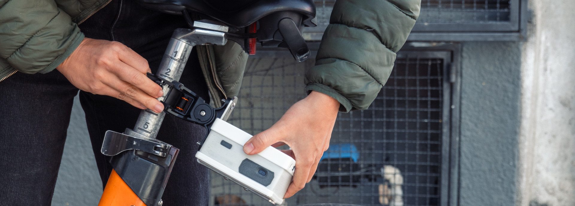 Close-up of hands fastening a white box beneath the seat of an orange bike